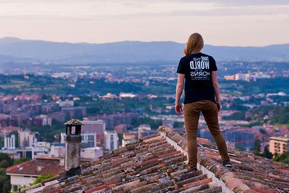 Student wearing t-shirt that reads "Take the world by the horns. Study abroad" standing on rooftop looking out over village